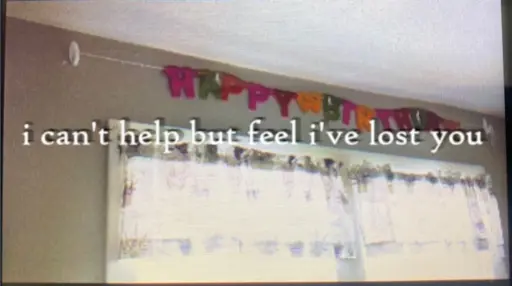 a colourful "happy birthday" decoration hanging above two windows. there's sunlight streaming through the curtains. the words "i can't help but feel i've lost you" are in shadowed white text